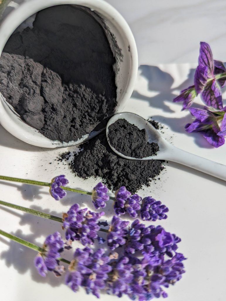 blackk powder on white dish and spoon with lavender flowers