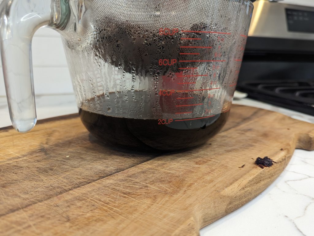 straining elderberry syrup into glass measuring cup