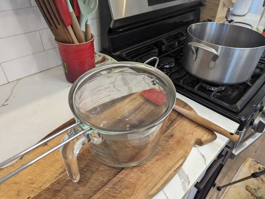measuring cup with strainer on top of wood cutting board in kitchen
