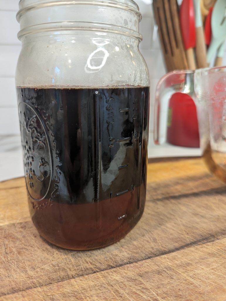 elderberry syrup mixing with honey in glass jar.