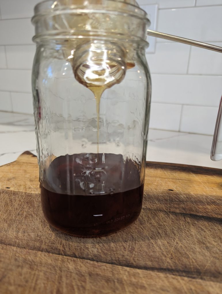 draining honey into mason jar on wood cutting board