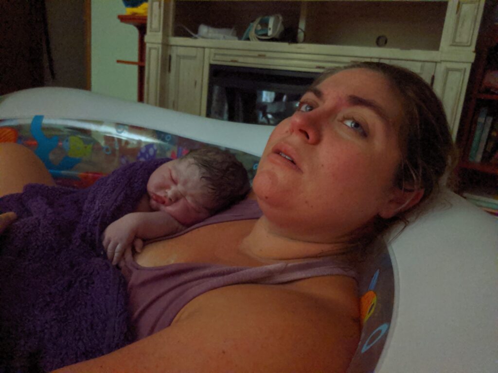 woman in birth pool with large newborn baby on chest