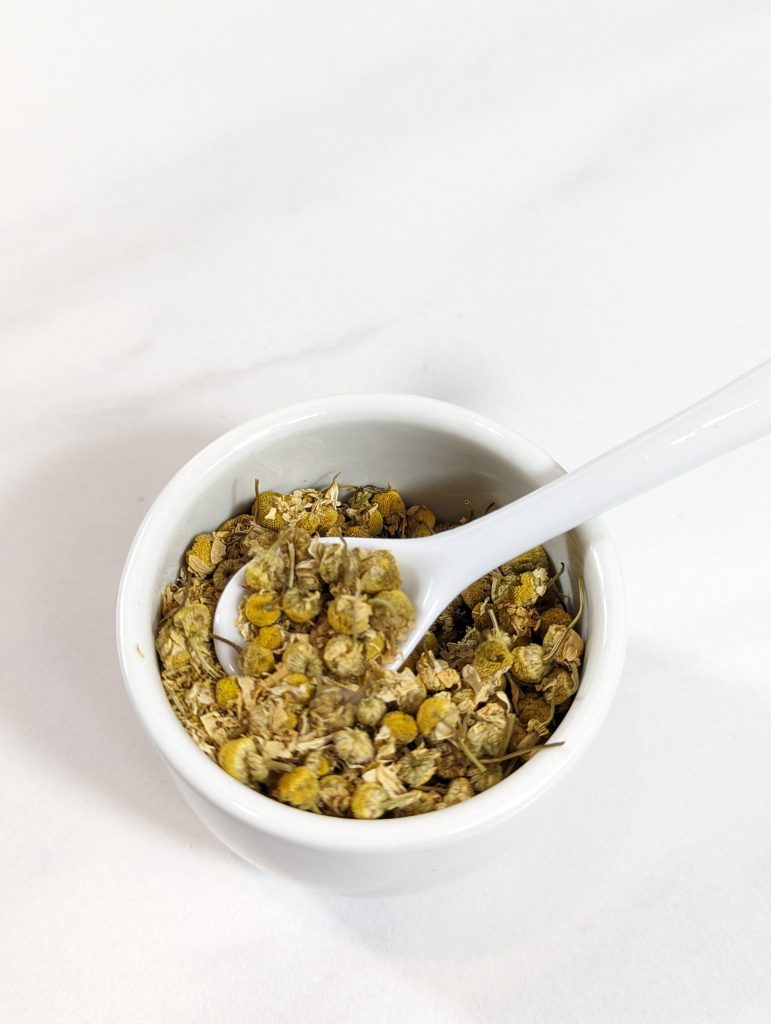 chamomile herb in white cup with spoon