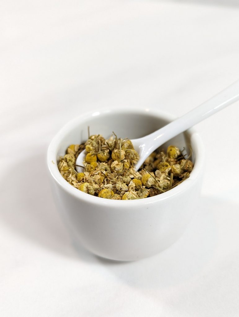 chamomile dried herb in white cup with white spoon