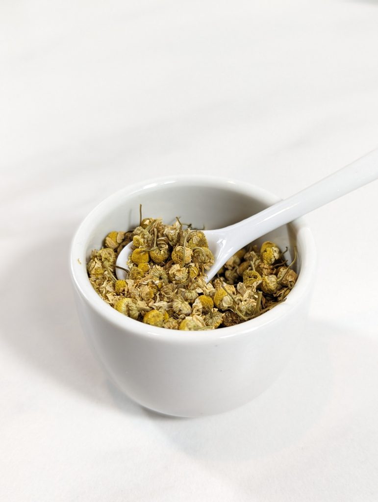 chamomile herb in white cup with spoon