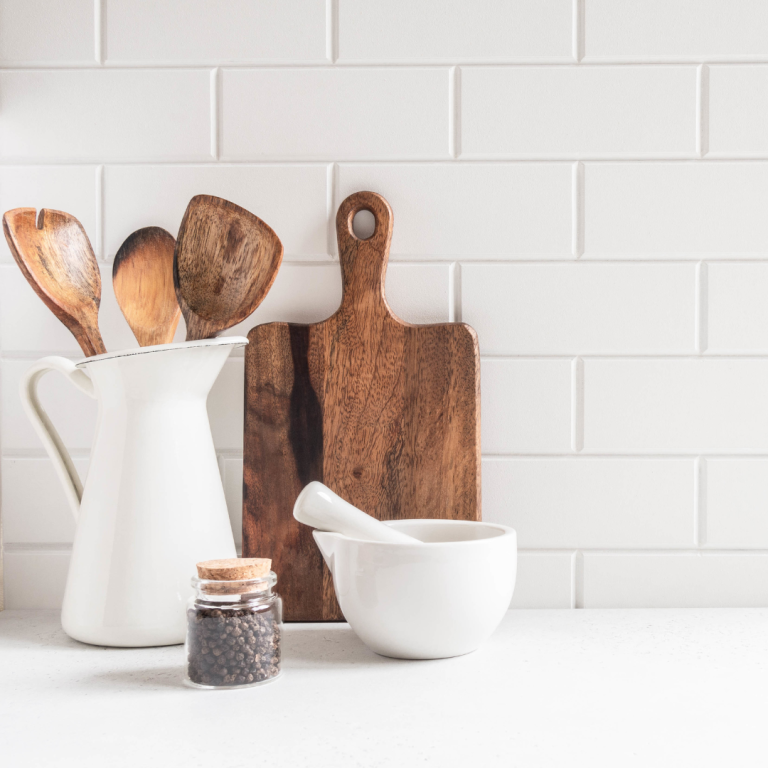 white kitchen counter and backsplash with wooden utensils and cutting board small jar and mortar and pestle.