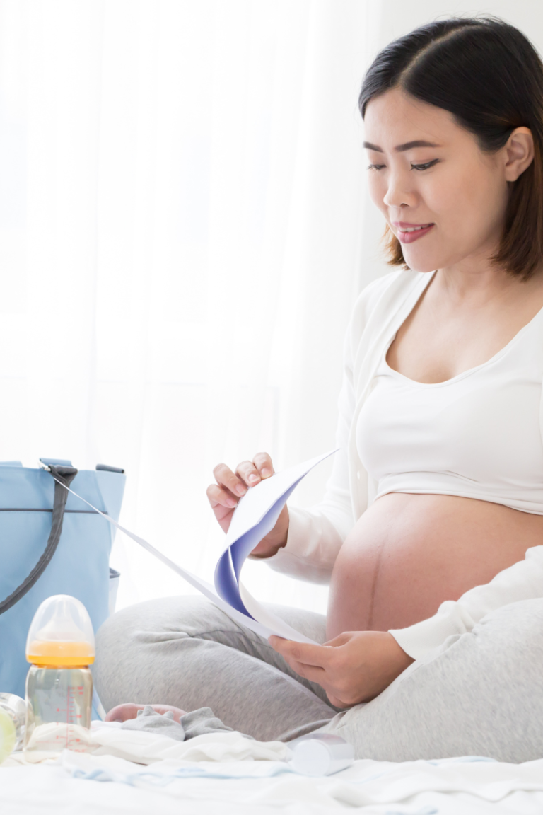pregnant woman with papers, bottle and a diaper bag on a bed