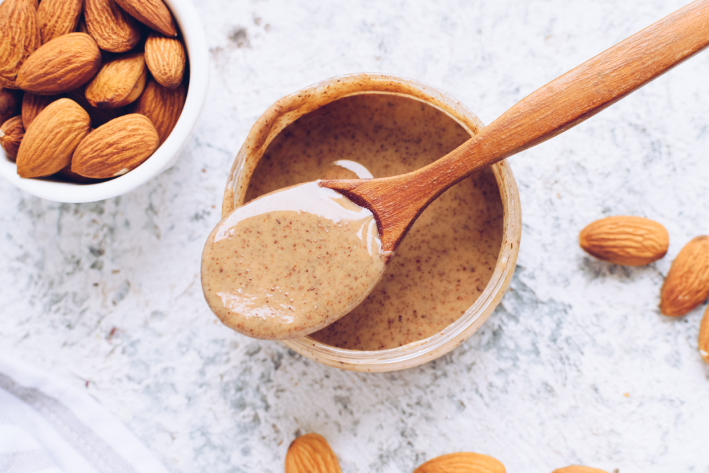 almond butter with wooden spoon and raw almonds