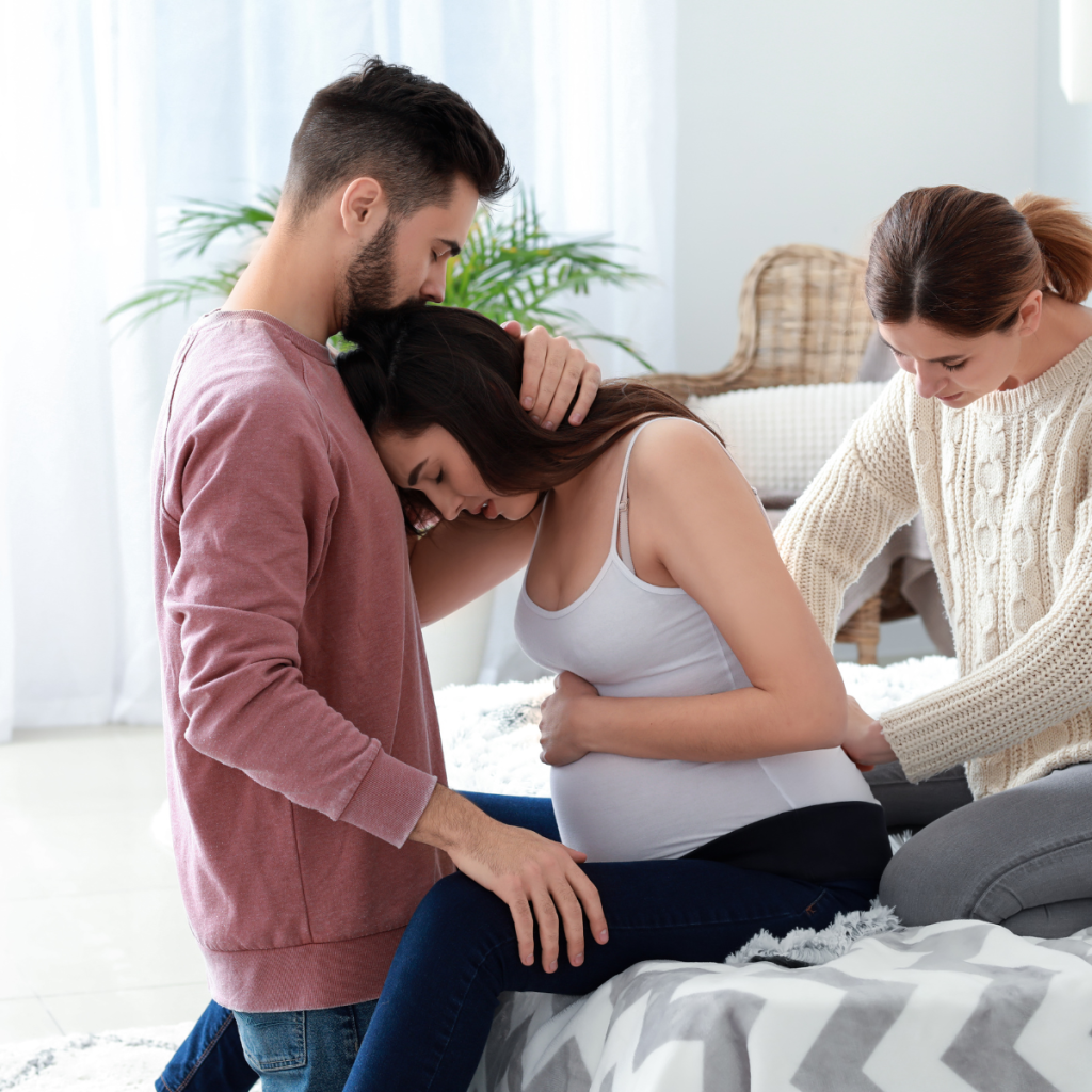 pregnant woman leaning on man while another woman rubs her low back