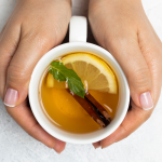 white mug with lemon slice and cinnamon stick with hands wrapping around the mug