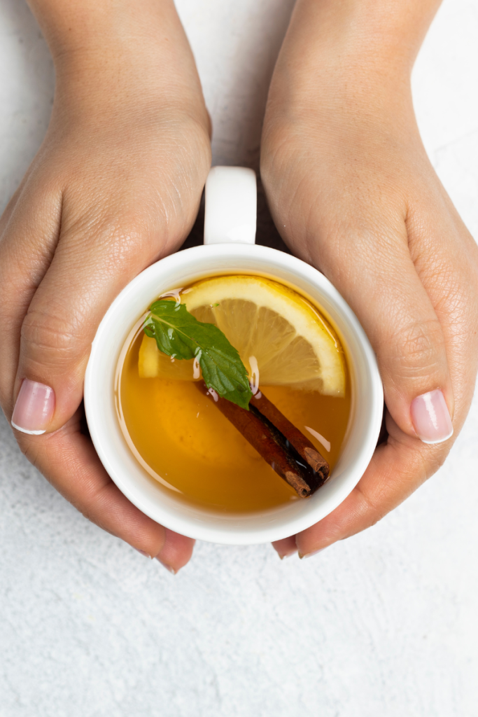 white mug with lemon slice and cinnamon stick with hands wrapping around the mug