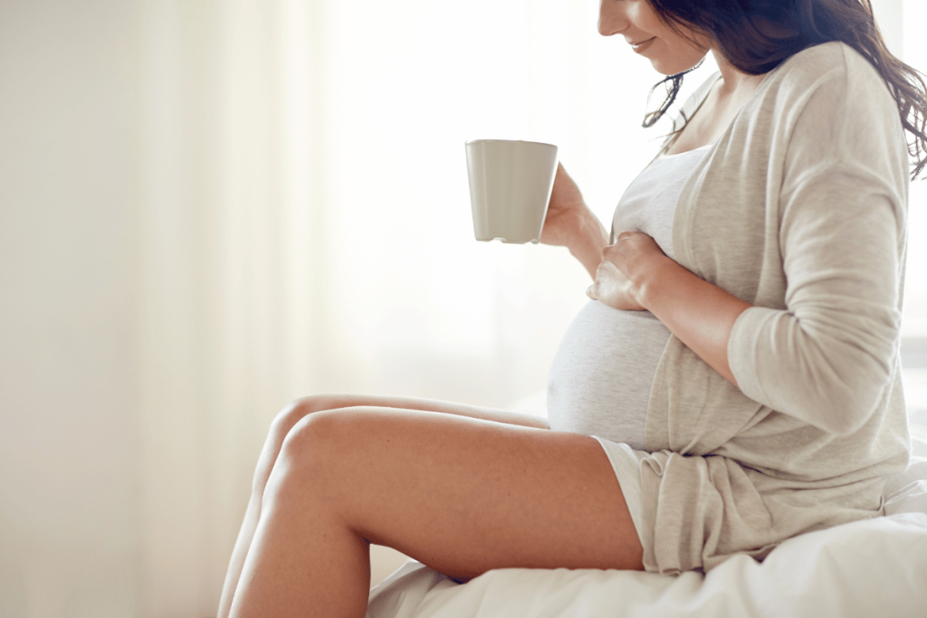 pregnant woman holding white mug of tea