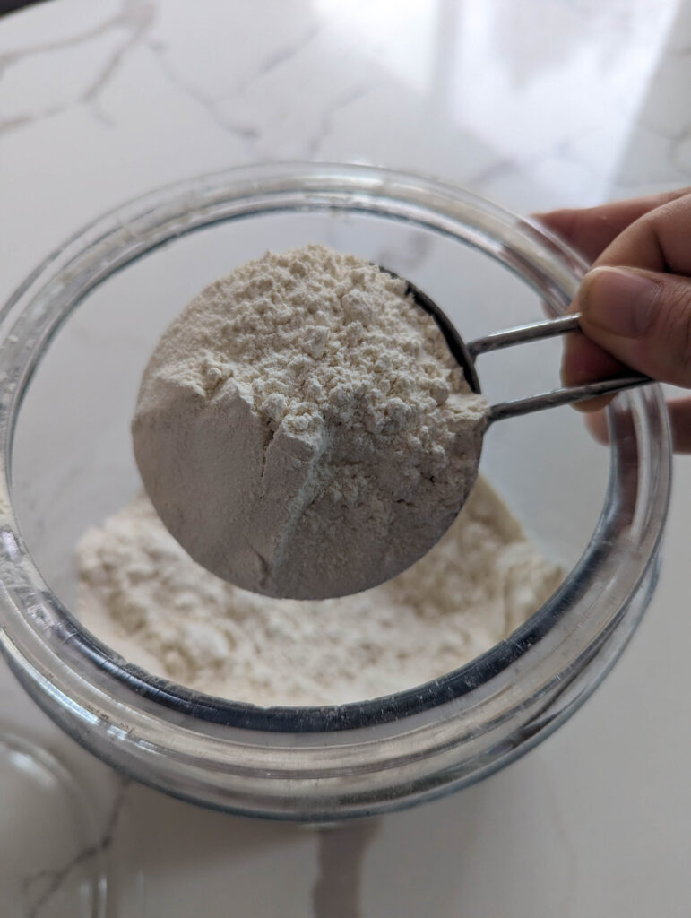 all purpose flour in glass jar and stainless steal measuring cup