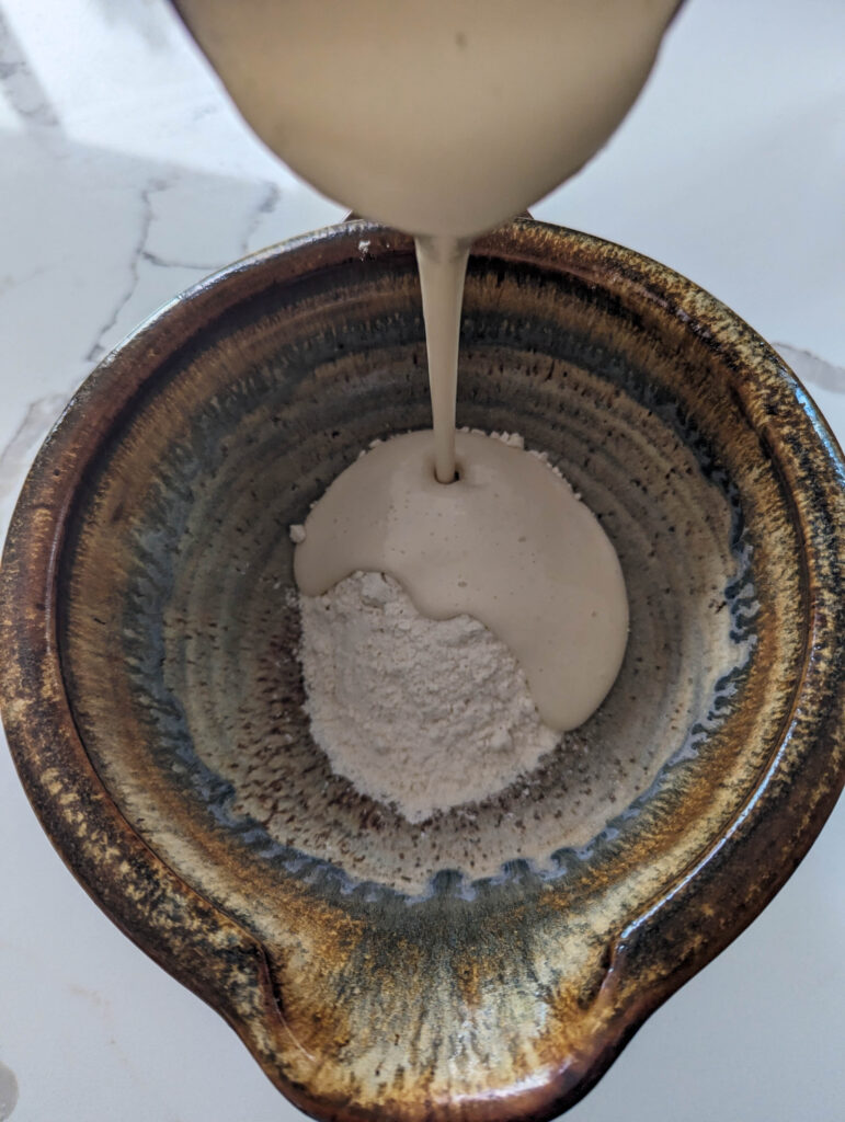 pouring sourdough starter onto flour in ceramic bowl