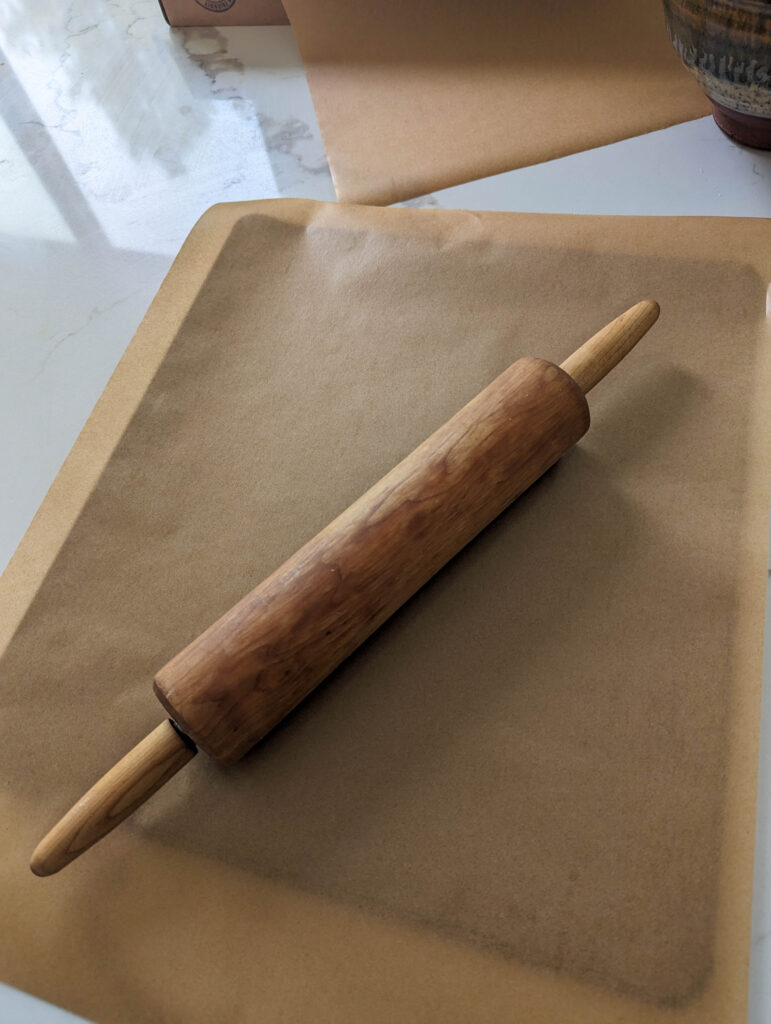 cookie sheet with parchment paper and wooden rolling pin on top of white counter