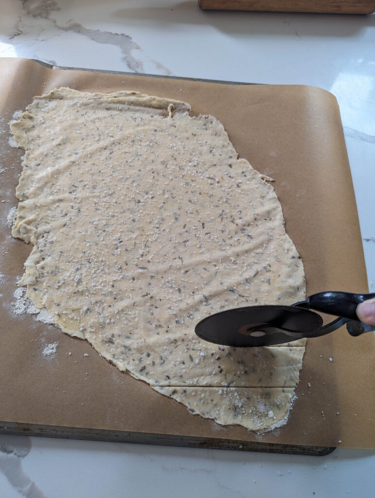 pizza cutter over sourdough herb cracker dough on parchment paper