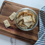 sourdough herb crackers on wooden cutting board with blue and white striped towel.