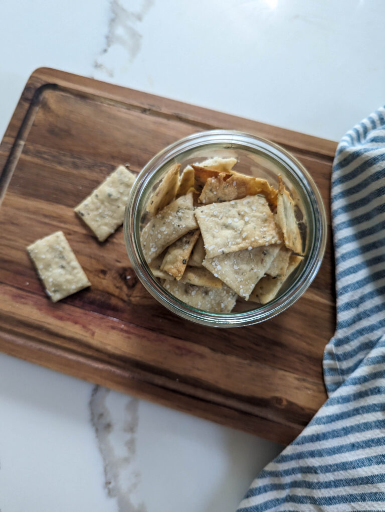 sourdough herb crackers on wooden cutting board with blue and white striped towel.