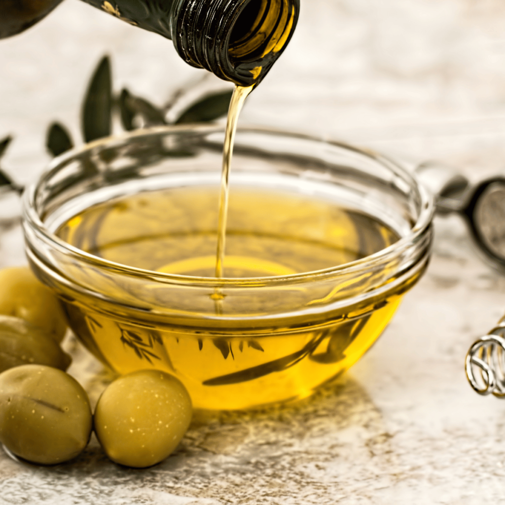 olive oil in glass bowl with green olives around