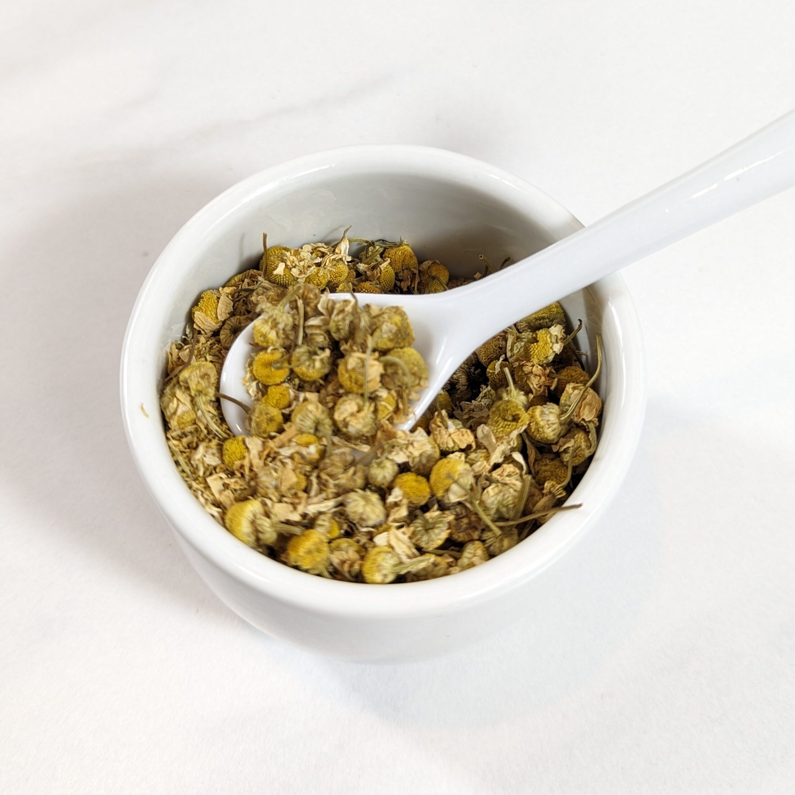 chamomile herb in white cup with spoon