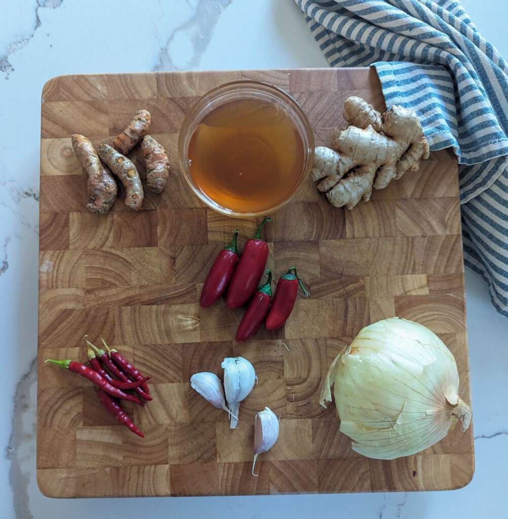 turmeric apple cider vinegar ginger root cayenne peppers japaleno peppers onion garlic on wood cutting board