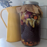 fire cider in mason jar on shite counter with yellow vase and eucalyptus