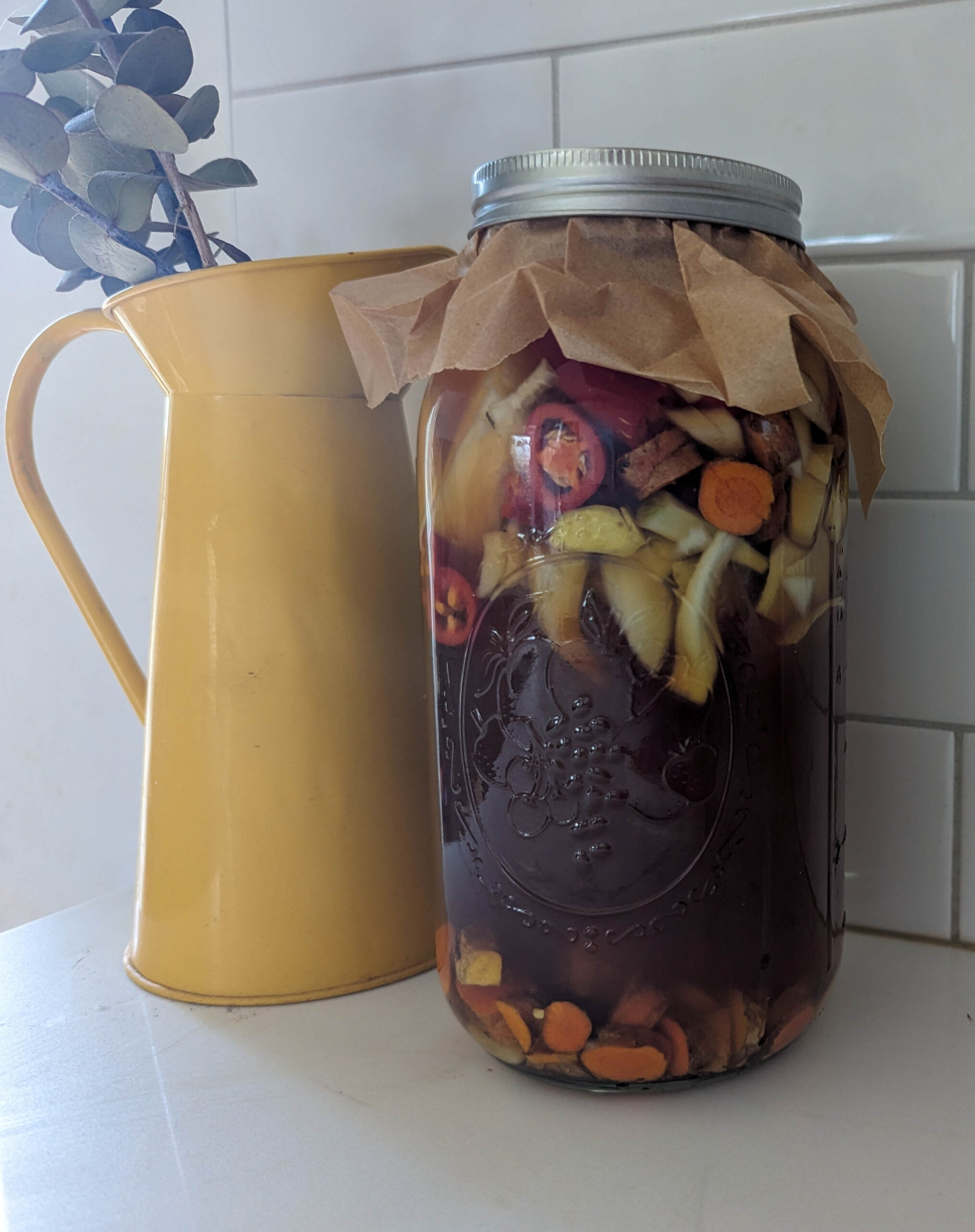 fire cider in mason jar on shite counter with yellow vase and eucalyptus