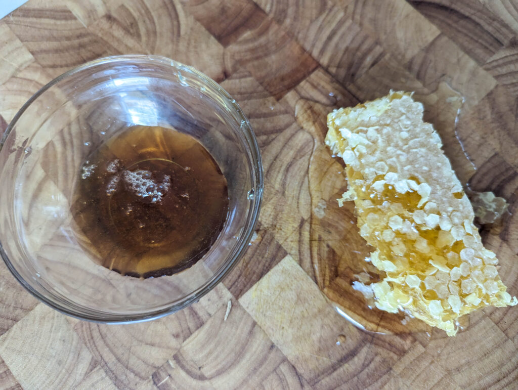 raw honey in a glass bowl and raw honey comb on wood cutting board