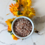 pink himalayan salt in white container with calendula flowers on white counter top