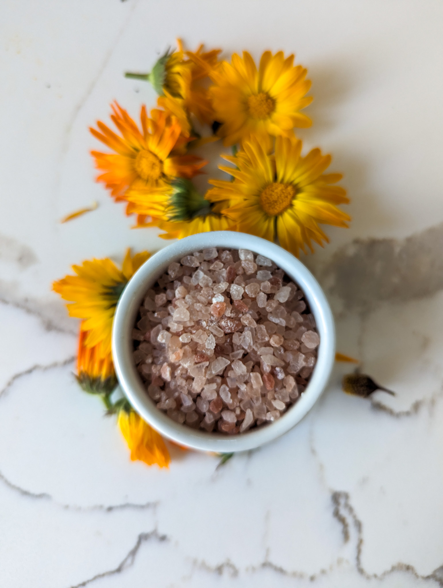 pink himalayan salt in white container with calendula flowers on white counter top