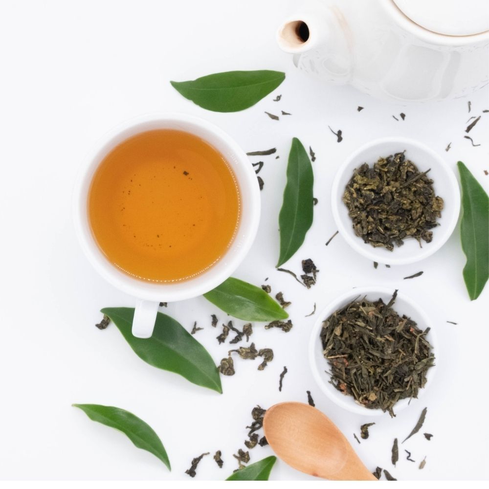 green tea vs herbal tea in a white tea cup with green leaves wooden spoon