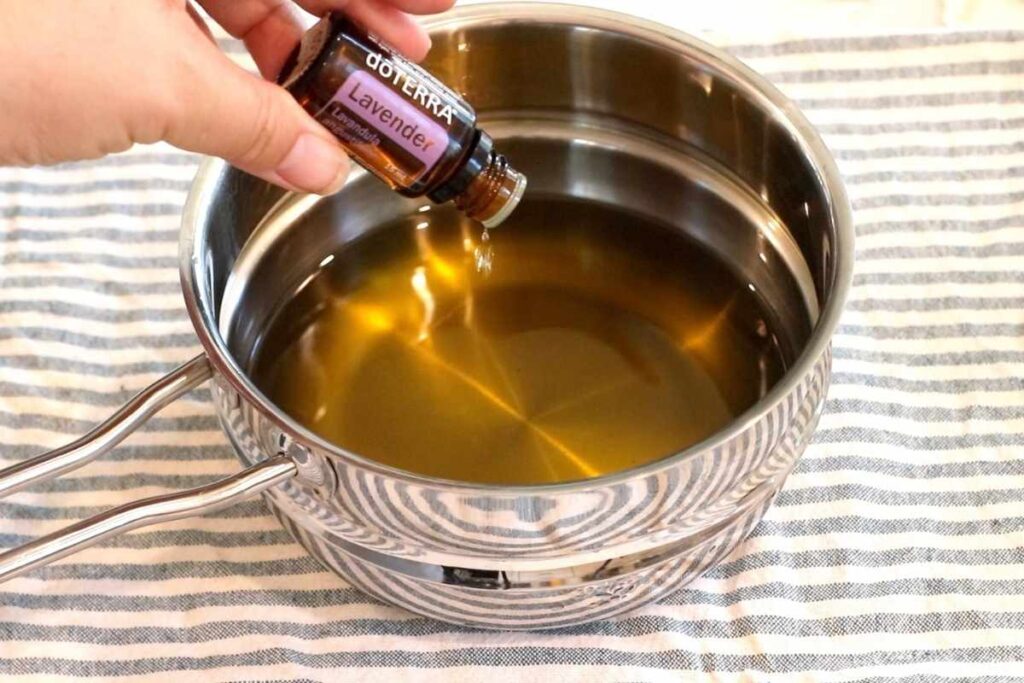 pouring lavender essential oil into herbal burn salve mixture in double boiler