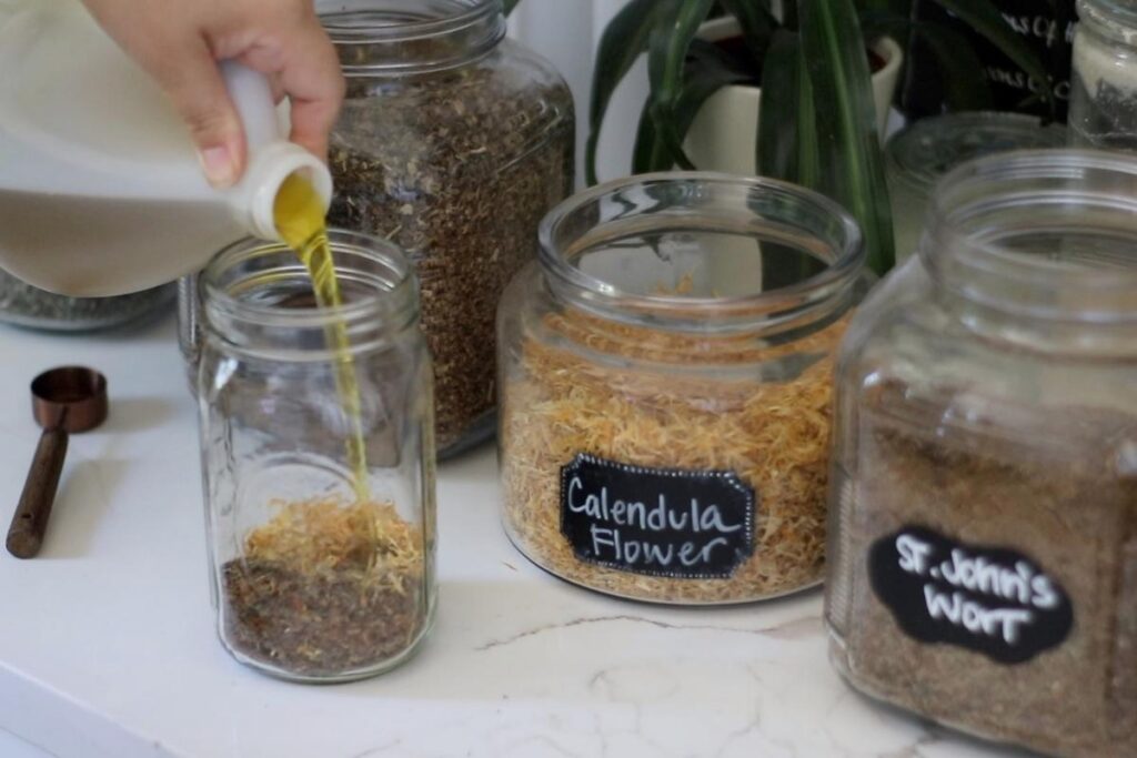 pouring olive oil over dried herbs for herbal burn salve recipe