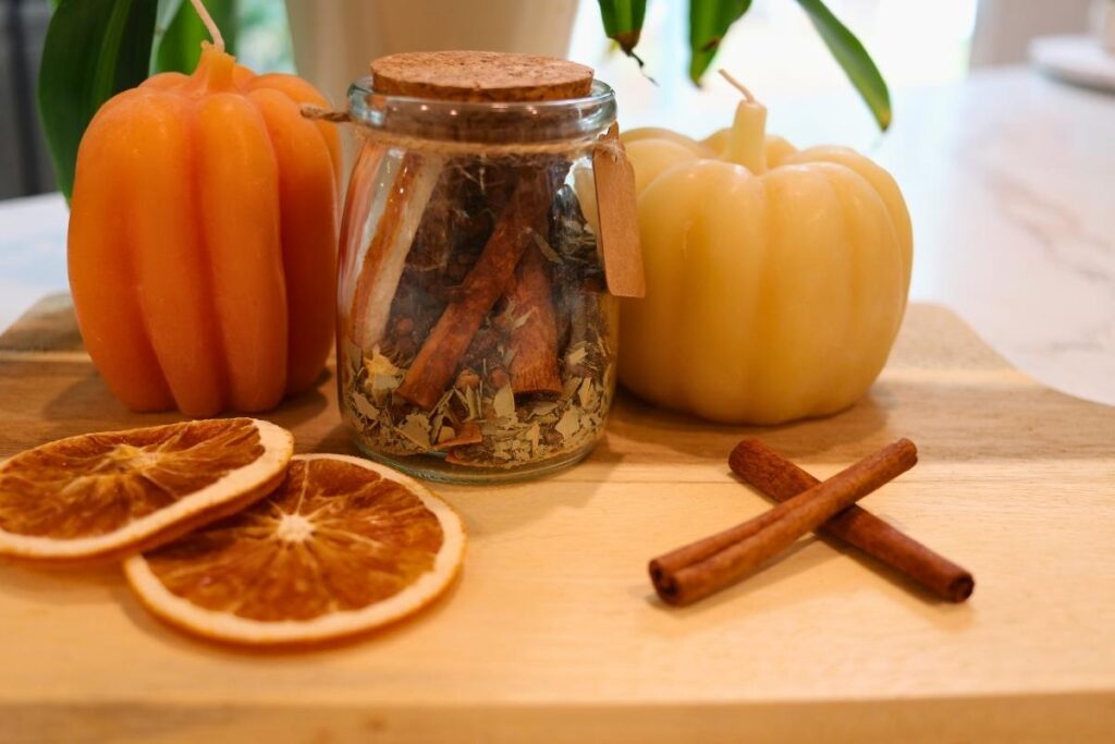 natural potpourri in white bowl with yellow and white pumpkin candle orange slices and cinnamon sticks