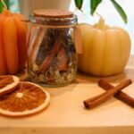 natural potpourri in white bowl with yellow and white pumpkin candle orange slices and cinnamon sticks