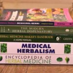 herbalism books on table top flanked by calendula and feverfew herbs in mason jars