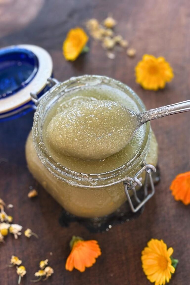 spooning up the calendula & chamomile body scrub with flowers on wooden cutting board