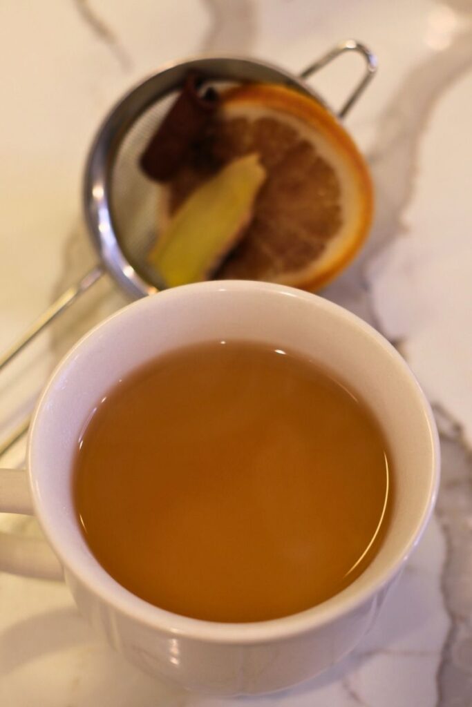 strained orange and clove spiced tea in white mug on counter