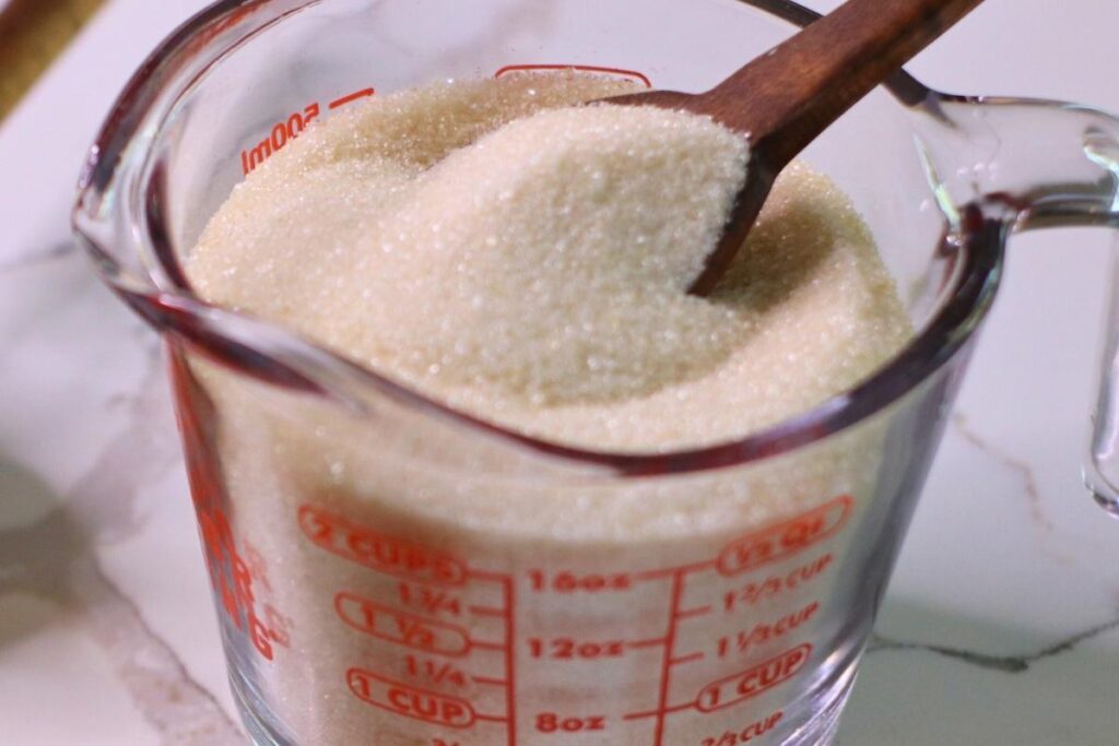 super fine sugar in glass measuring cup with wooden spoon