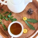 dandelion flowers leaf and nettle with tea in white tea cup on top of basket